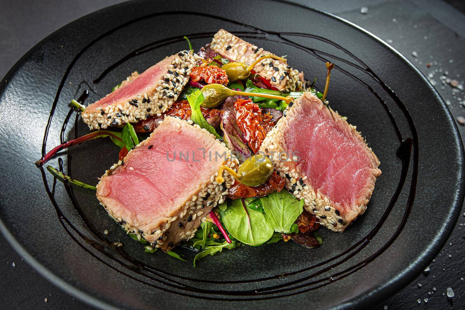 Close up of tuna slices withsesam seeds and fresh vegetables on a dark plate. Top view