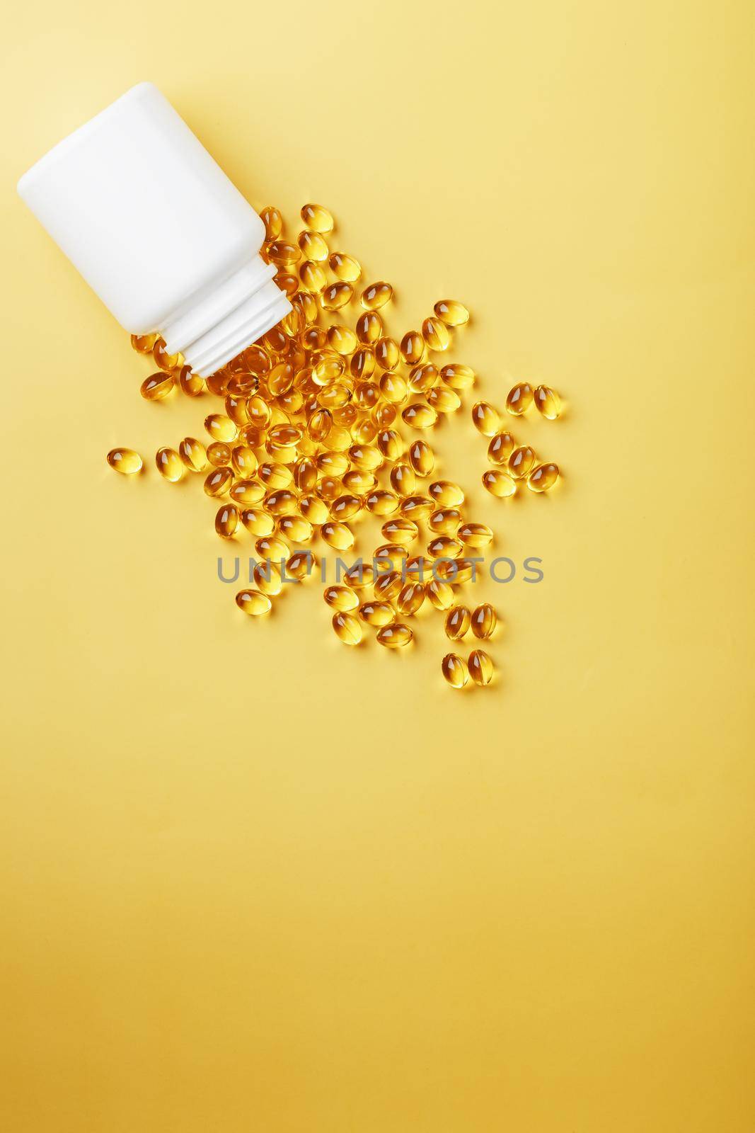 Golden Omega-3 fish oil capsules poured out of a jar on a yellow background. Free space