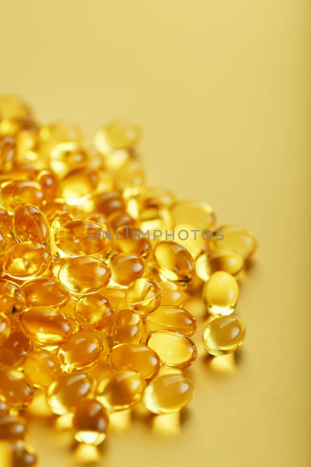 Pile of golden capsules of vitamin D3 on a yellow background with free space by AlexGrec