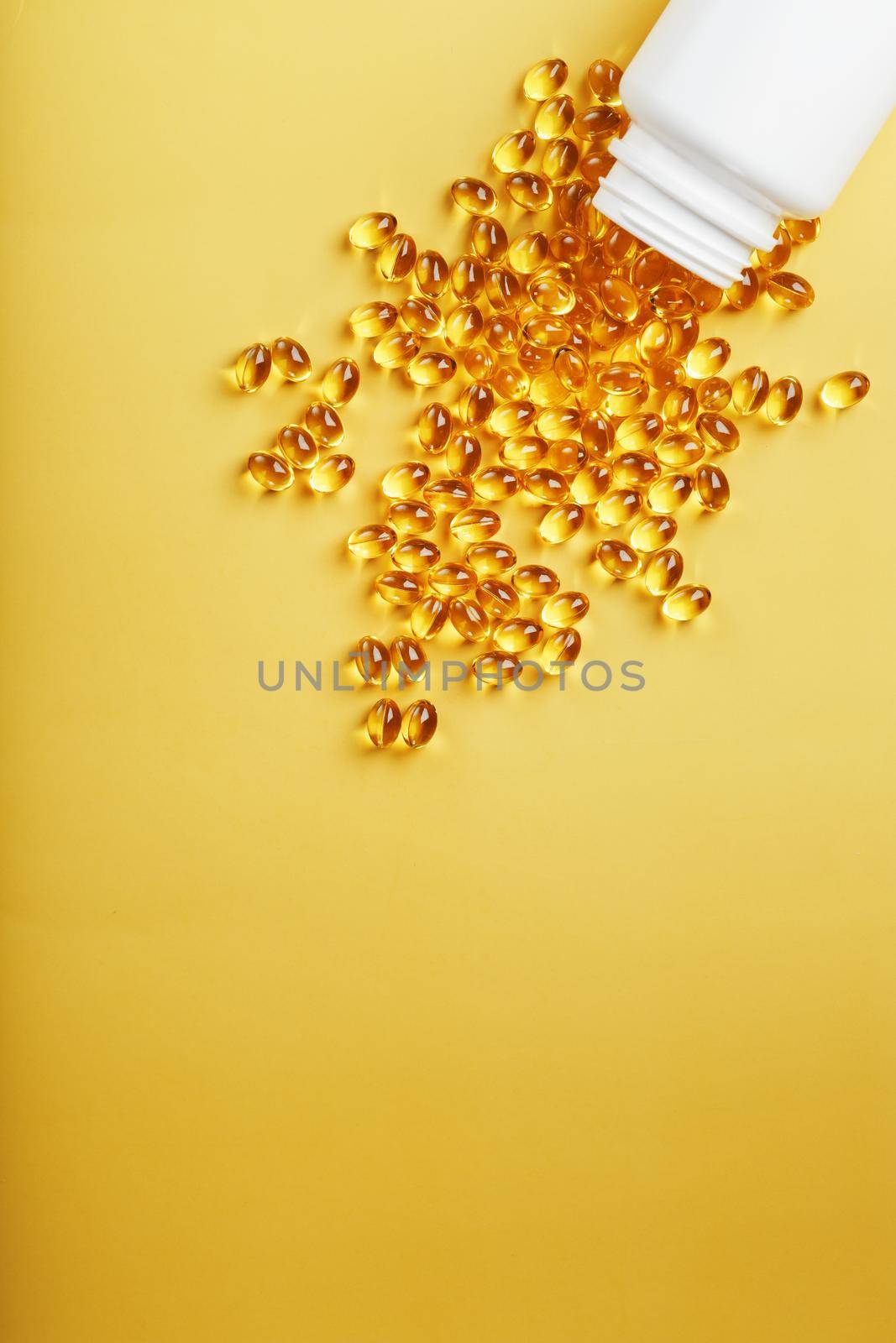Gold Vitamin D3 capsules poured out of a jar on a yellow background with free space. The most important vitamin in an easily digestible liquid form.