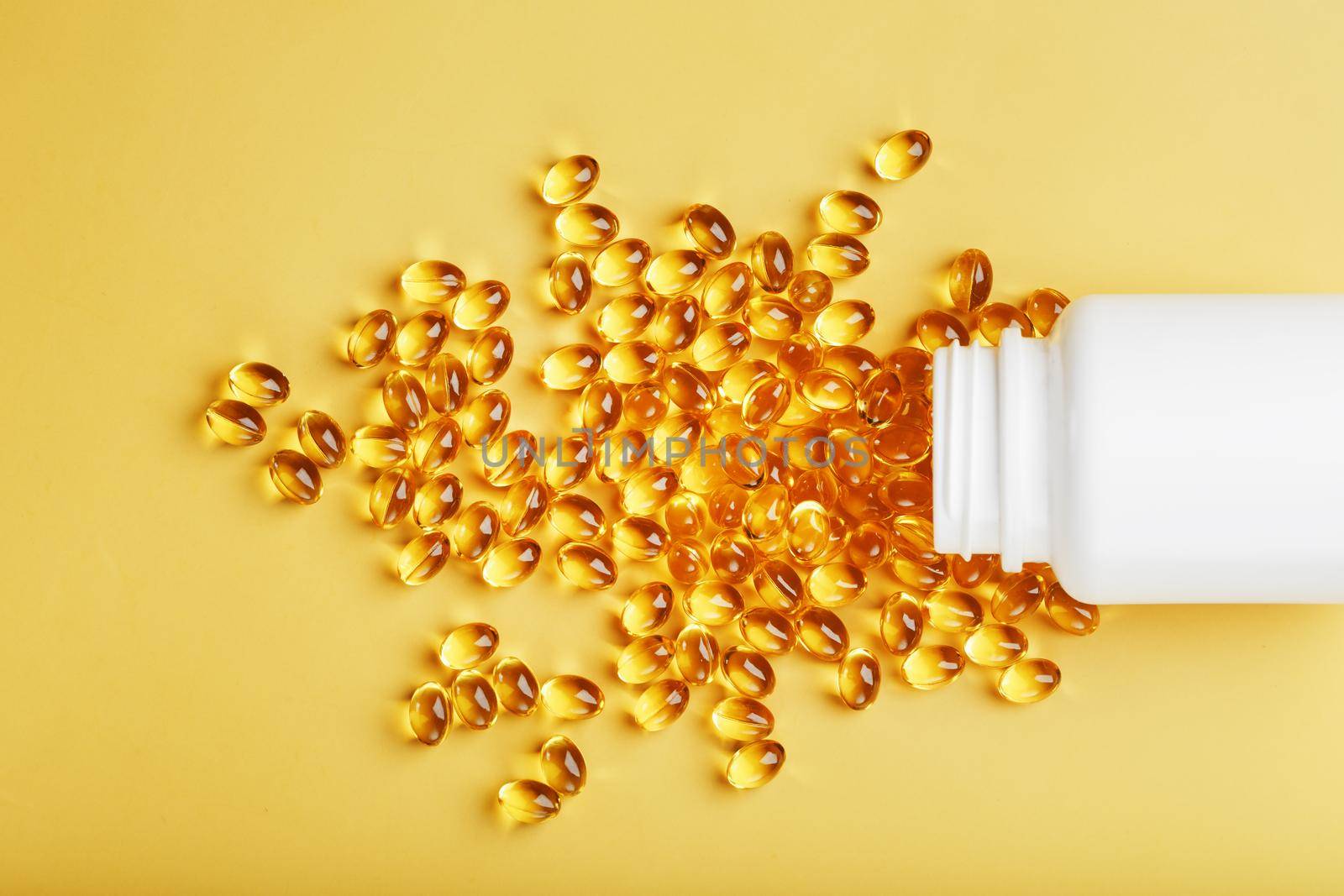 Gold Vitamin D3 capsules poured out of a jar on a yellow background with free space. The most important vitamin in an easily digestible liquid form.