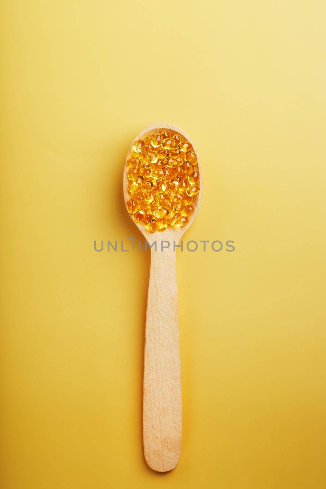 Vitamin D3 Capsules in a spoon with other vitamin D3 capsules around them on a yellow background by AlexGrec