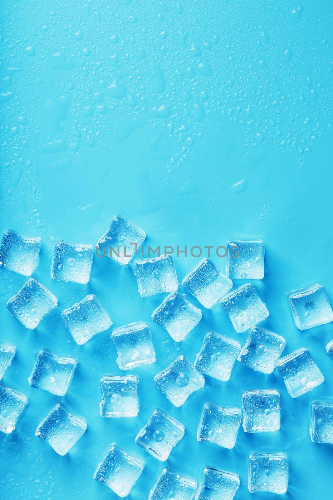 Ice cubes with water drops scattered on a blue background, top view