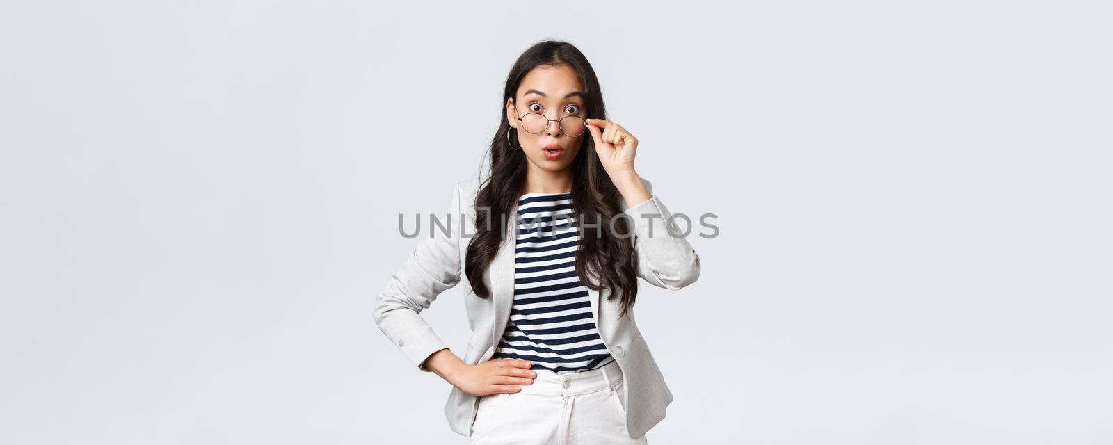 Business, finance and employment, female successful entrepreneurs concept. Shocked asian office lady take-off glasses and widen eyes as hear big news, gasping amazed, stand white background.