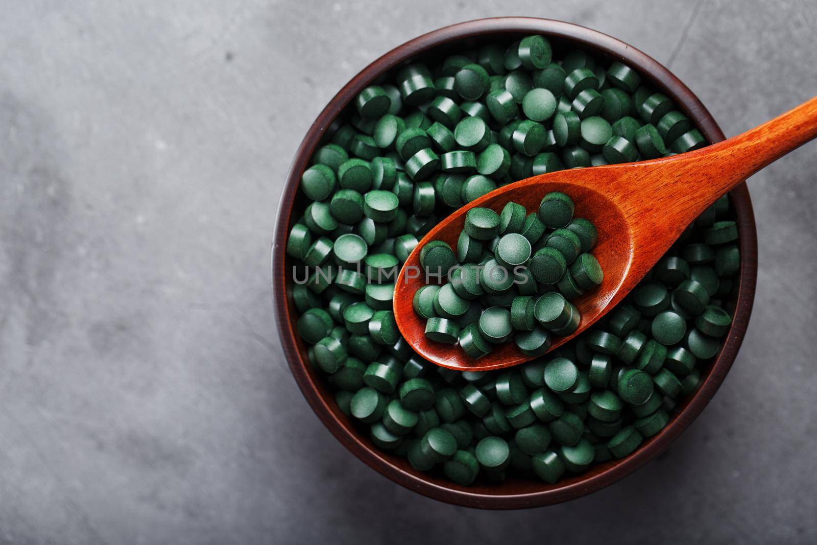 Vitamins from spirulina in a wooden cup with a wooden spoon on a dark background. Vegetarian source of amino acids and omega 3