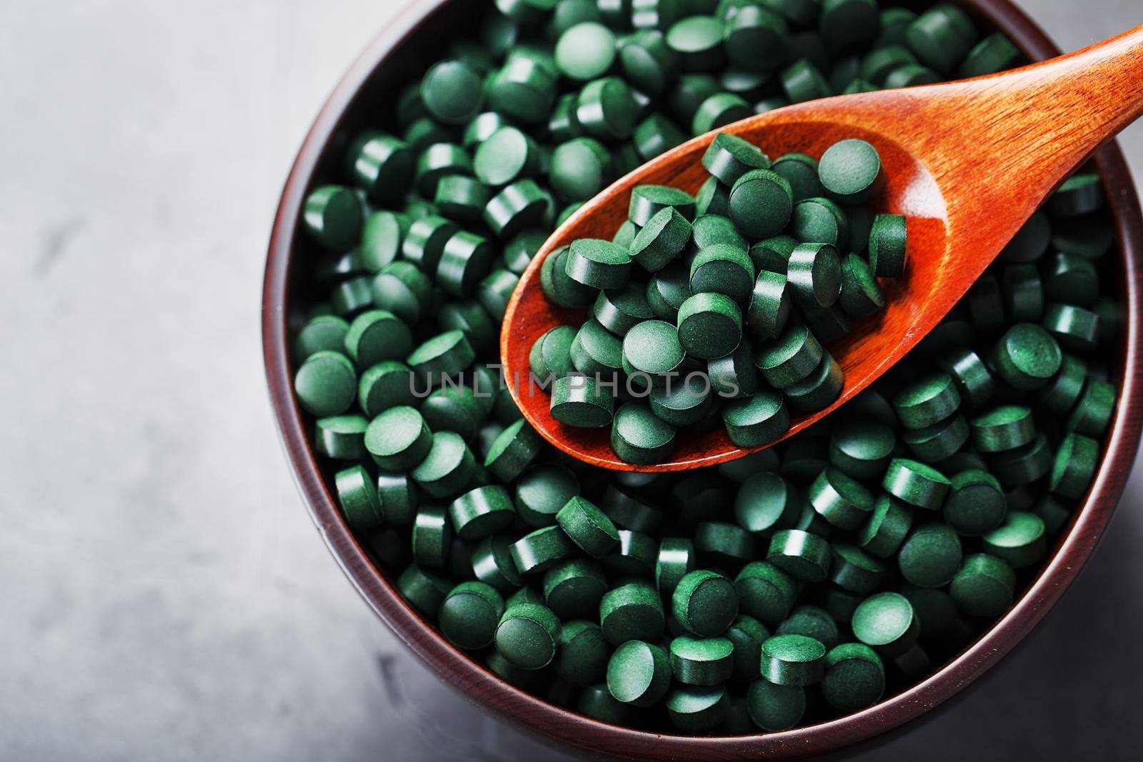 Vitamins from spirulina in a wooden cup with a wooden spoon on a dark background. Vegetarian source of amino acids and omega 3