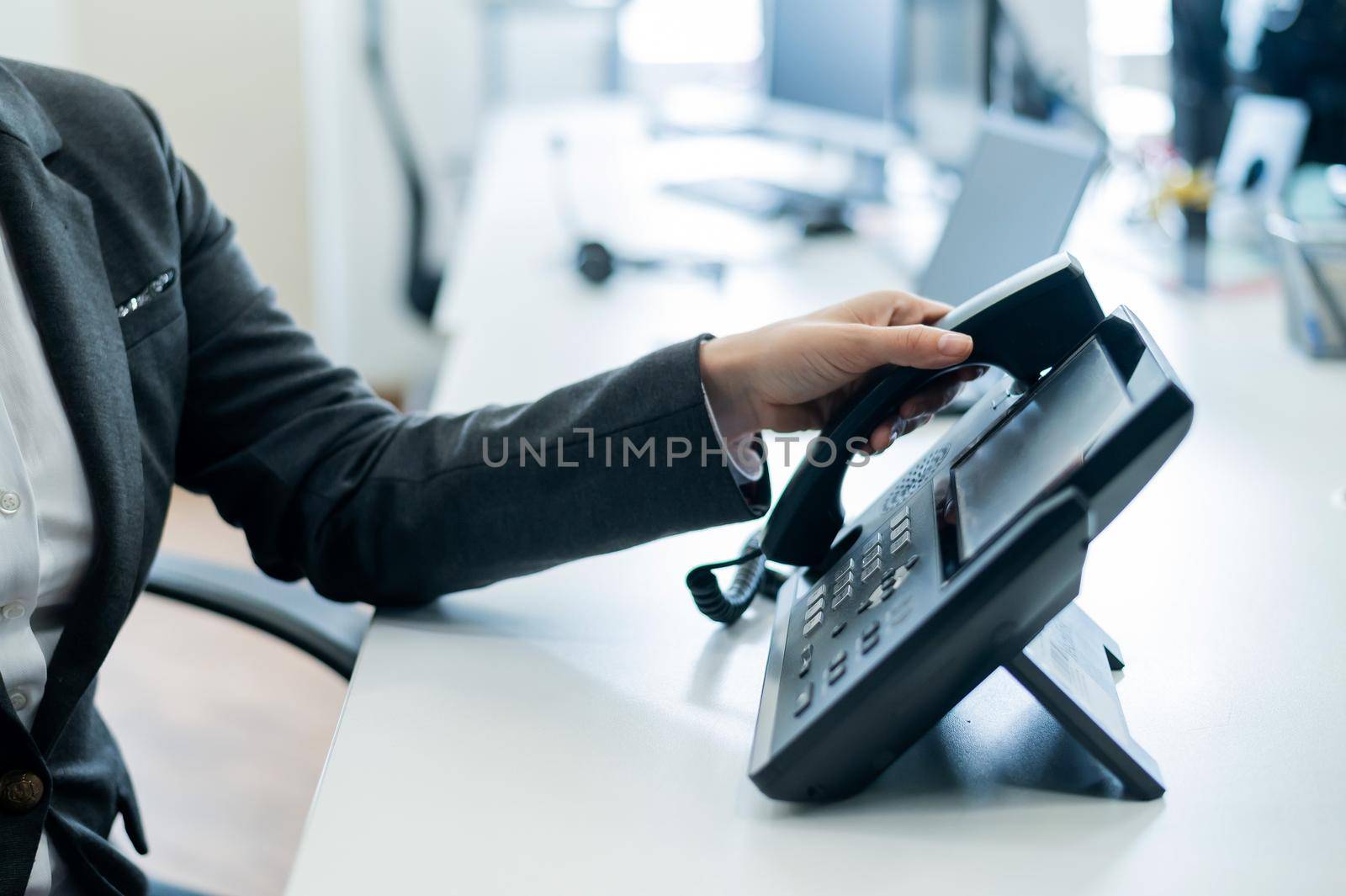 Closeup female hand on landline phone in office. Faceless woman in a suit works as a receptionist answering the phone to customer calls. by mrwed54