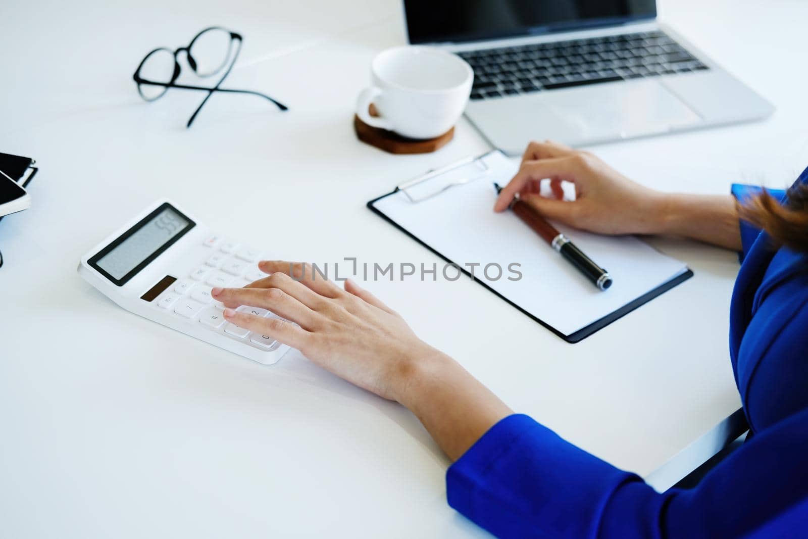 A female company employee is using a calculator to calculate sales income on a tablet computer screen via the Internet. by Manastrong