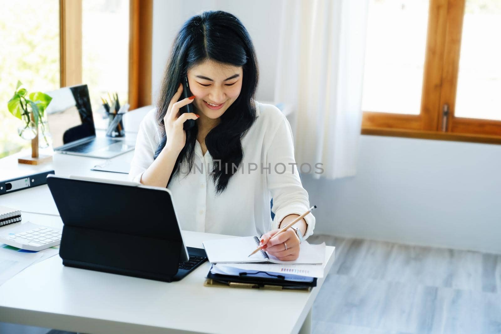 business dealings, an Asian company secretary is on the phone with customers comes to contact with using pen to write down the time to summarize the schedule for work the owner of the company