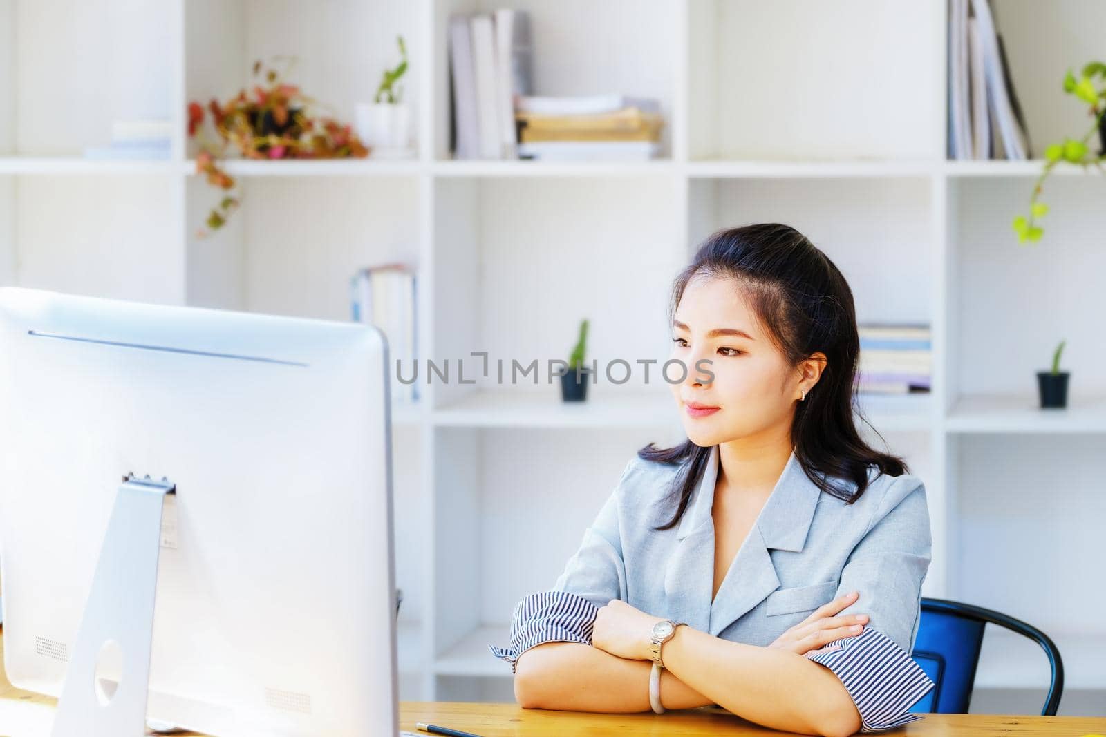 An Asian entrepreneur or businesswoman shows a smiling face while working with using computer on a wooden table. by Manastrong