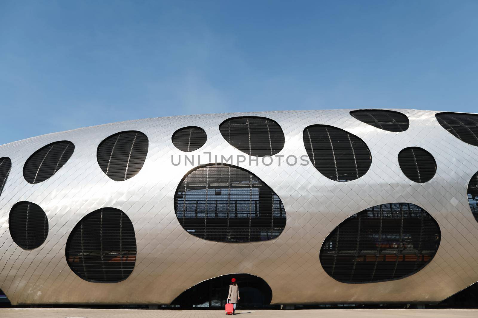 young woman with a red travel suitcase by the futuristic facade of modern architecture. Travel