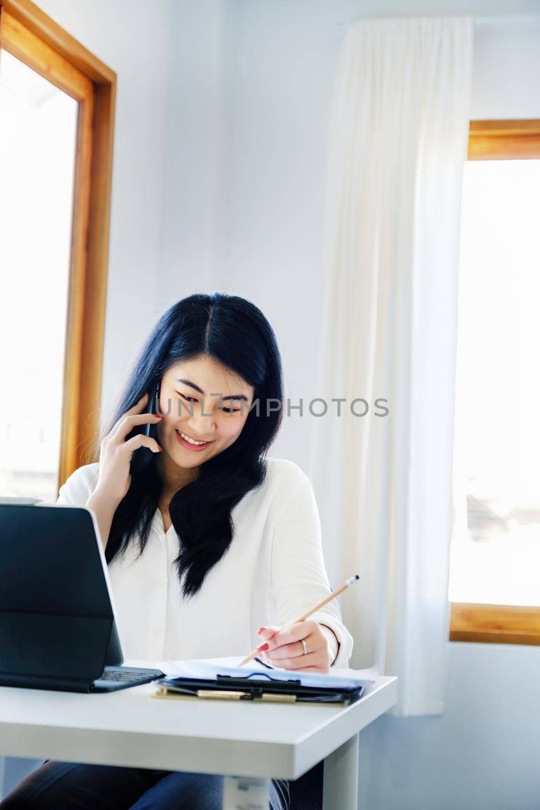 business dealings, an Asian company secretary is on the phone with customers comes to contact with using pen to write down the time to summarize the schedule for work the owner of the company