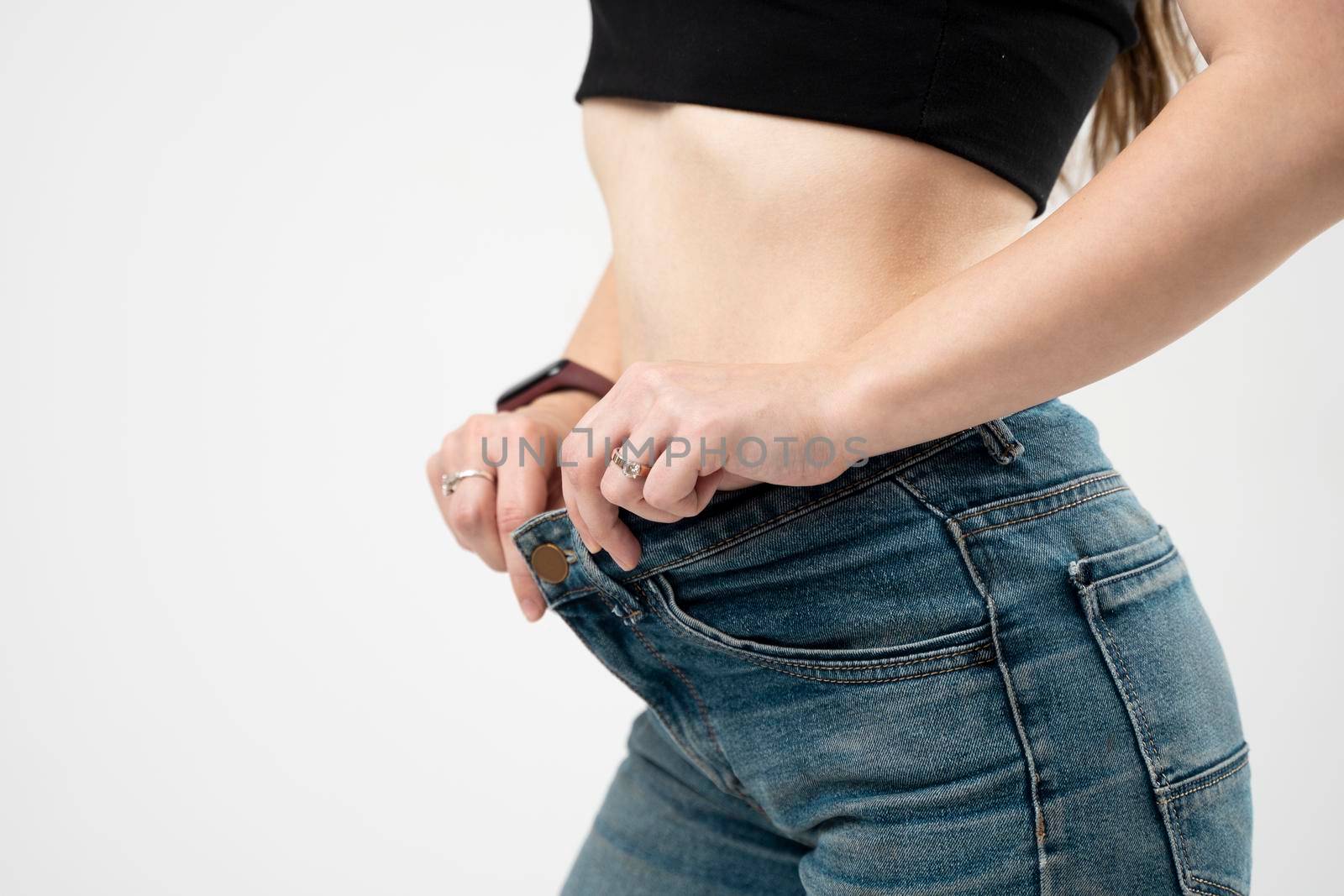 Slim sporty woman in blue jeans showing a result of weight loss on white background. Diet concept and weight loss