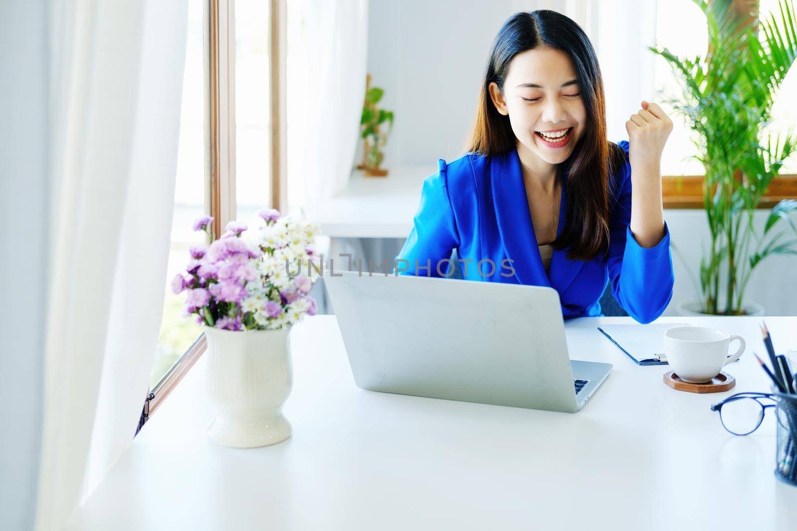 Business finance and investment, a business woman expresses happiness after successfully investing in the stock market on the Internet through a computer placed on a desk