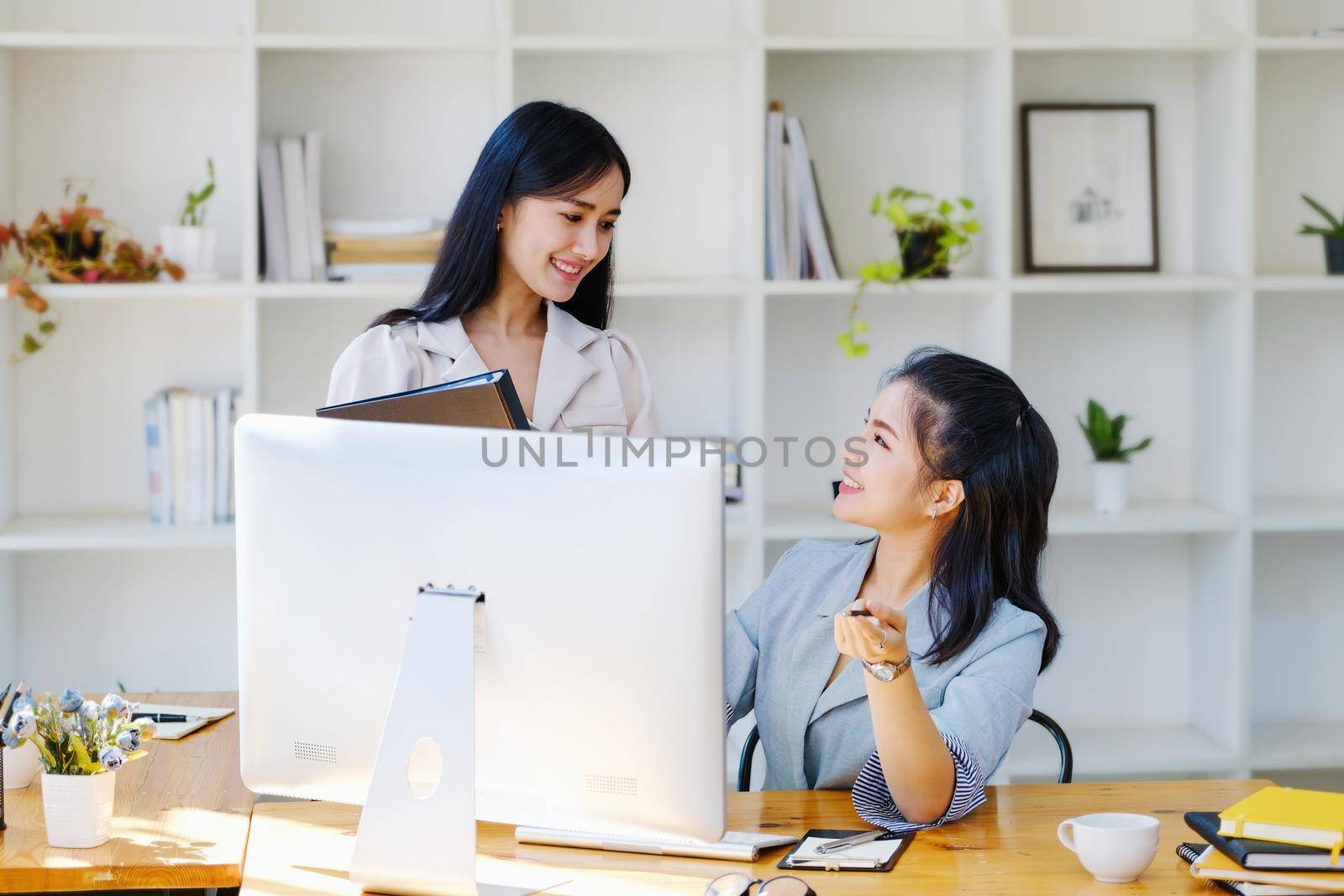 Consultation, discussion, marketing and investment concept, female employee pointing at computer monitor and colleague holding folder to draw conclusions and assess investment risks for the company