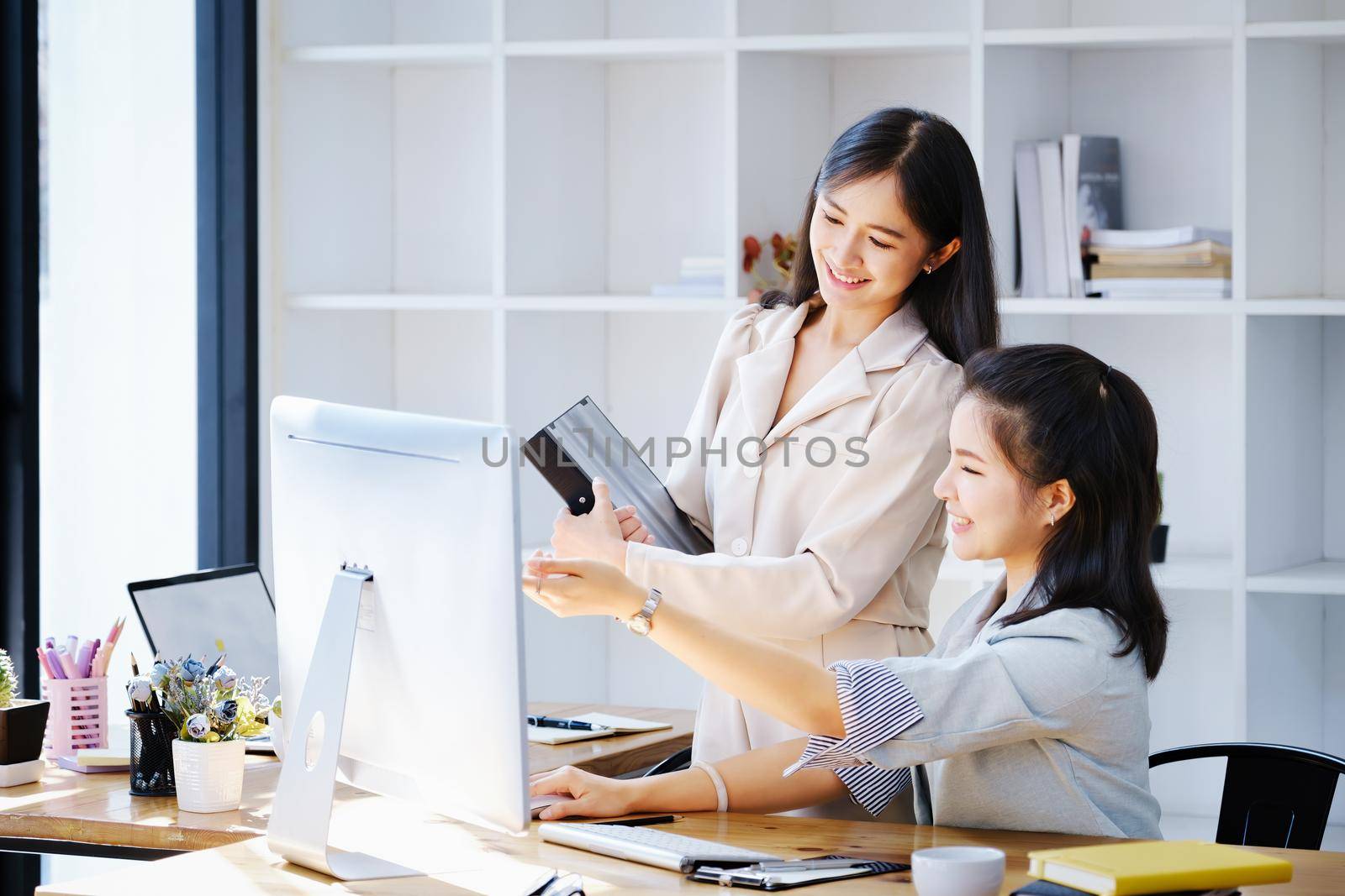 Consultation, discussion, marketing and investment concept, female employee holding folder and colleague pointing at a computer monitor to draw conclusions and assess investment risks for the company