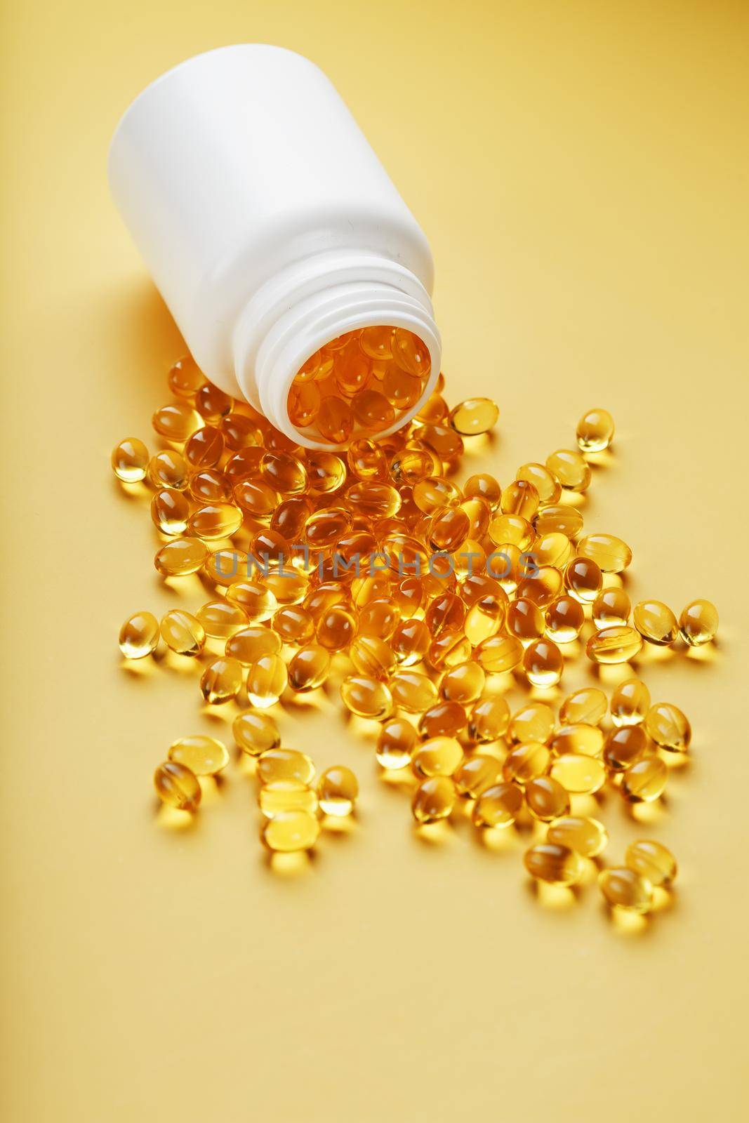 Gold Vitamin D3 capsules poured out of a jar on a yellow background with free space. The most important vitamin in an easily digestible liquid form.