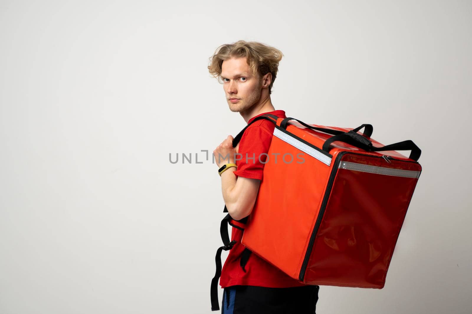 Delivery Service Cocnept. Courier wearing red uniform and thermo backpack bag looking at camera isolated on white studio background