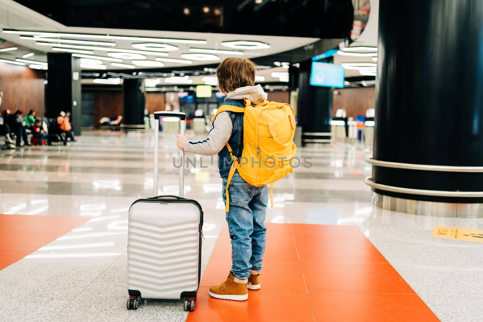 Child boy with backpack standing in the airport terminal, waiting for flight, travel with suitcase. Vacation concept.