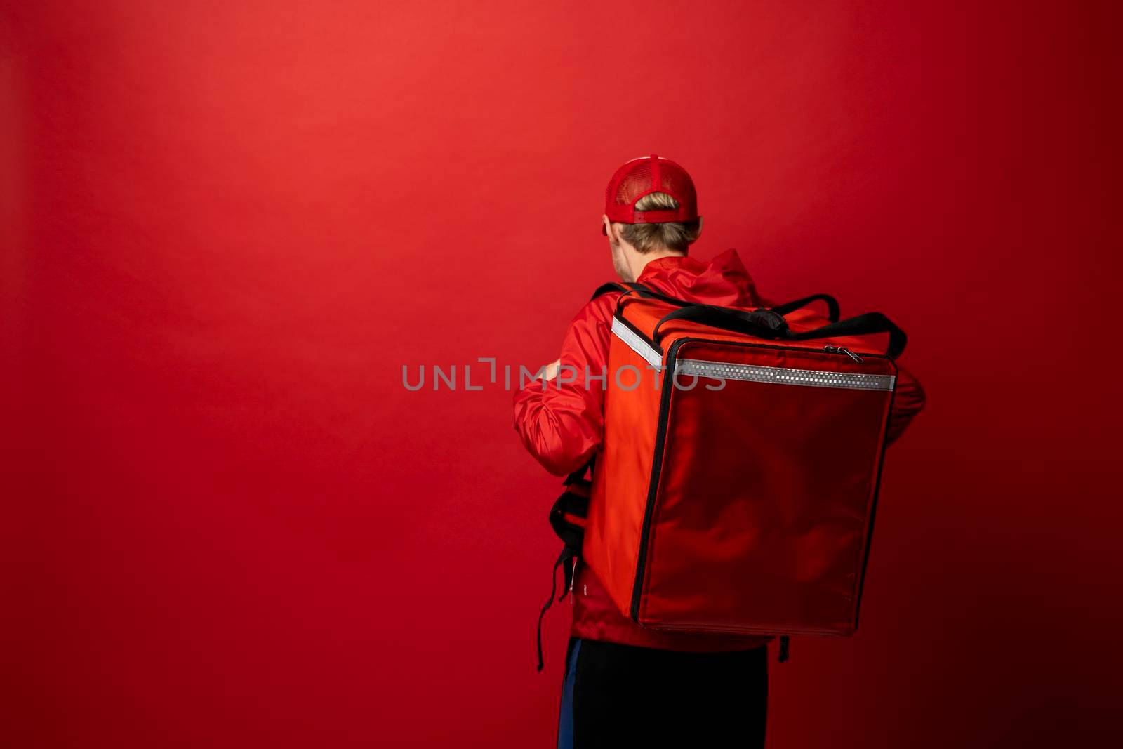 Delivery man in red uniform with a thermal backpack isolated on a white background. Fast home delivery. Online order. Courier delivers groceries home. by vovsht