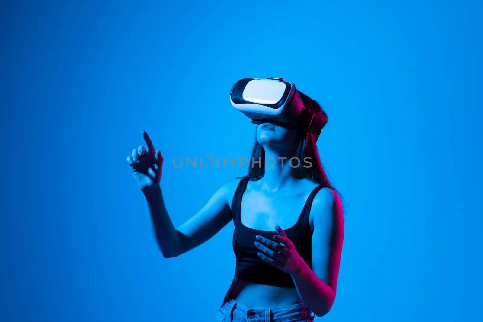 Close up of young woman stands in studio wearing VR glasses and swiping scrolling zooming with hands in a virtual space while interacting with a objects in a metaverse. Virtual reality technology. by vovsht