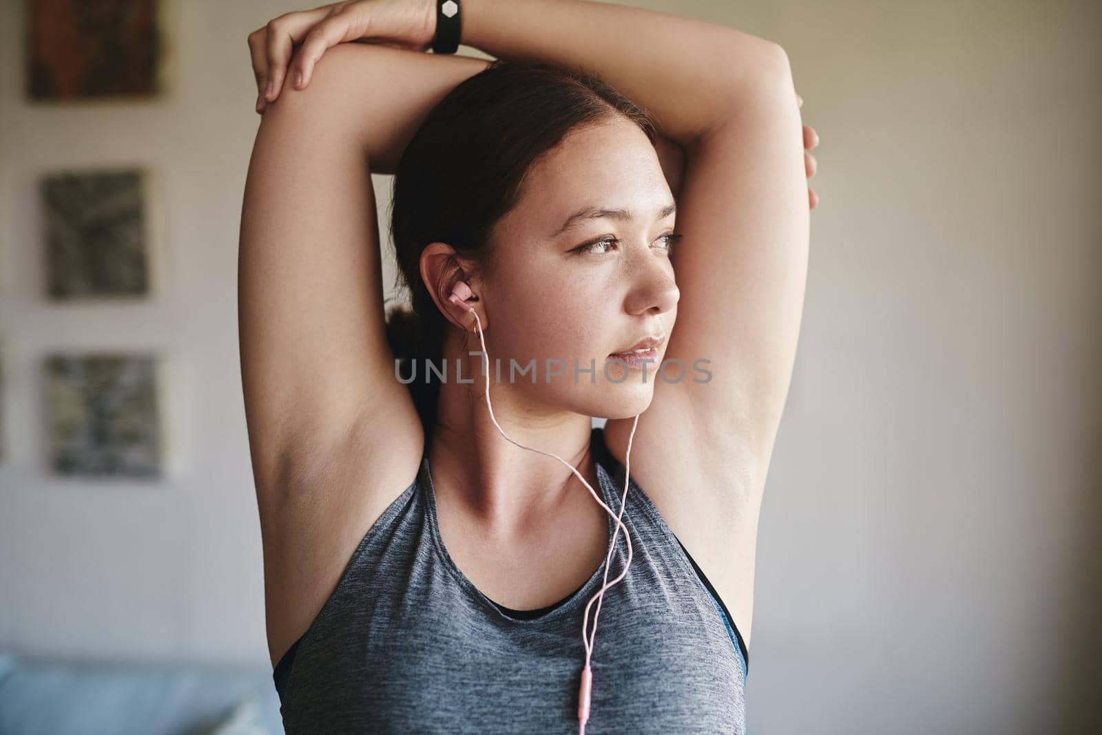 Cropped shot of an attractive young woman standing in her room and stretching her tricep after a workout at home.