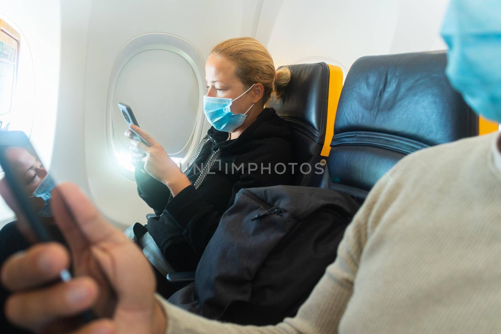 A young couple wearing face mask, using smart phone while traveling on airplane. New normal travel after covid-19 pandemic concept. by kasto