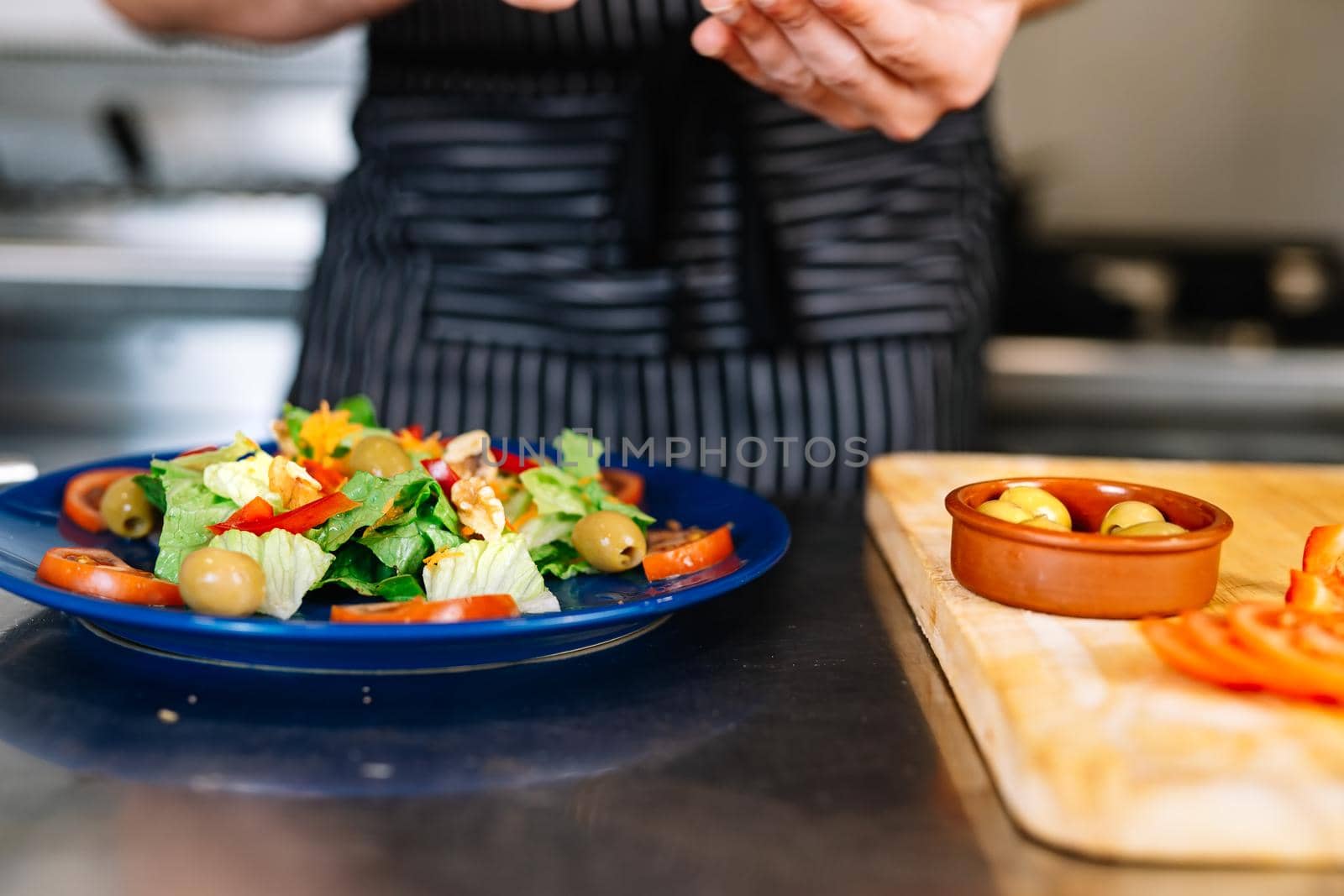 Detail of the hands of a young boss, putting ingredients on a salad plate in a professional kitchen. by CatPhotography