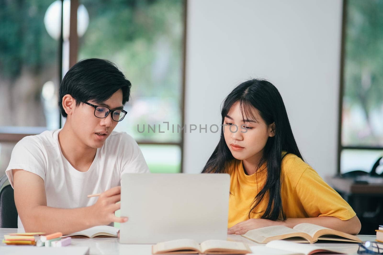 Learning, education and school concept. Young woman and man studying for a test or an exam. Tutor books with friends. Young students campus helps friend catching up and learning.