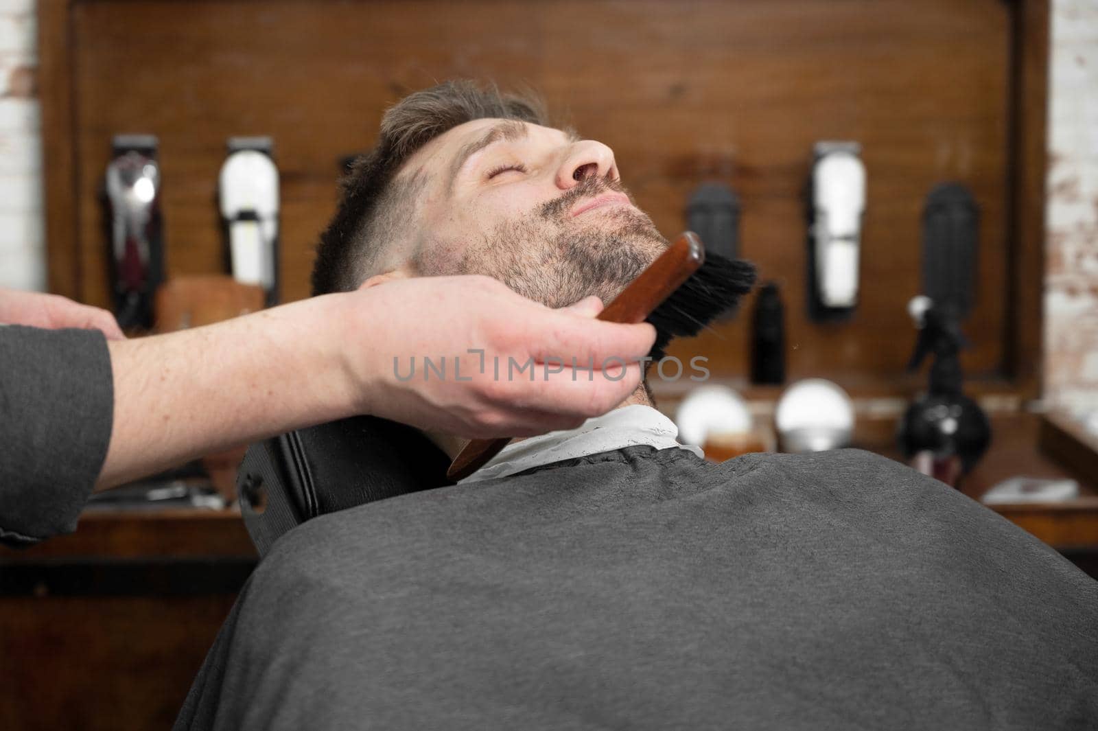 Shot of a barber using a brush on his client's beard by HERRAEZ