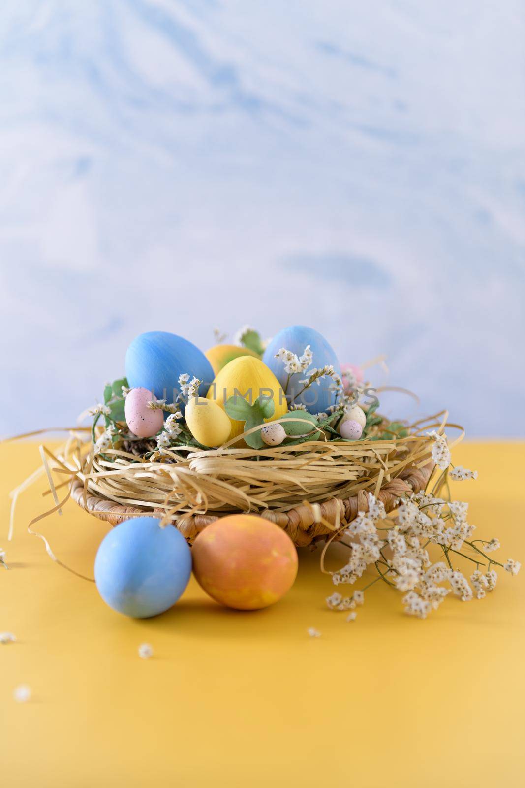 Easter eggs in nest on blue background and yellow table.