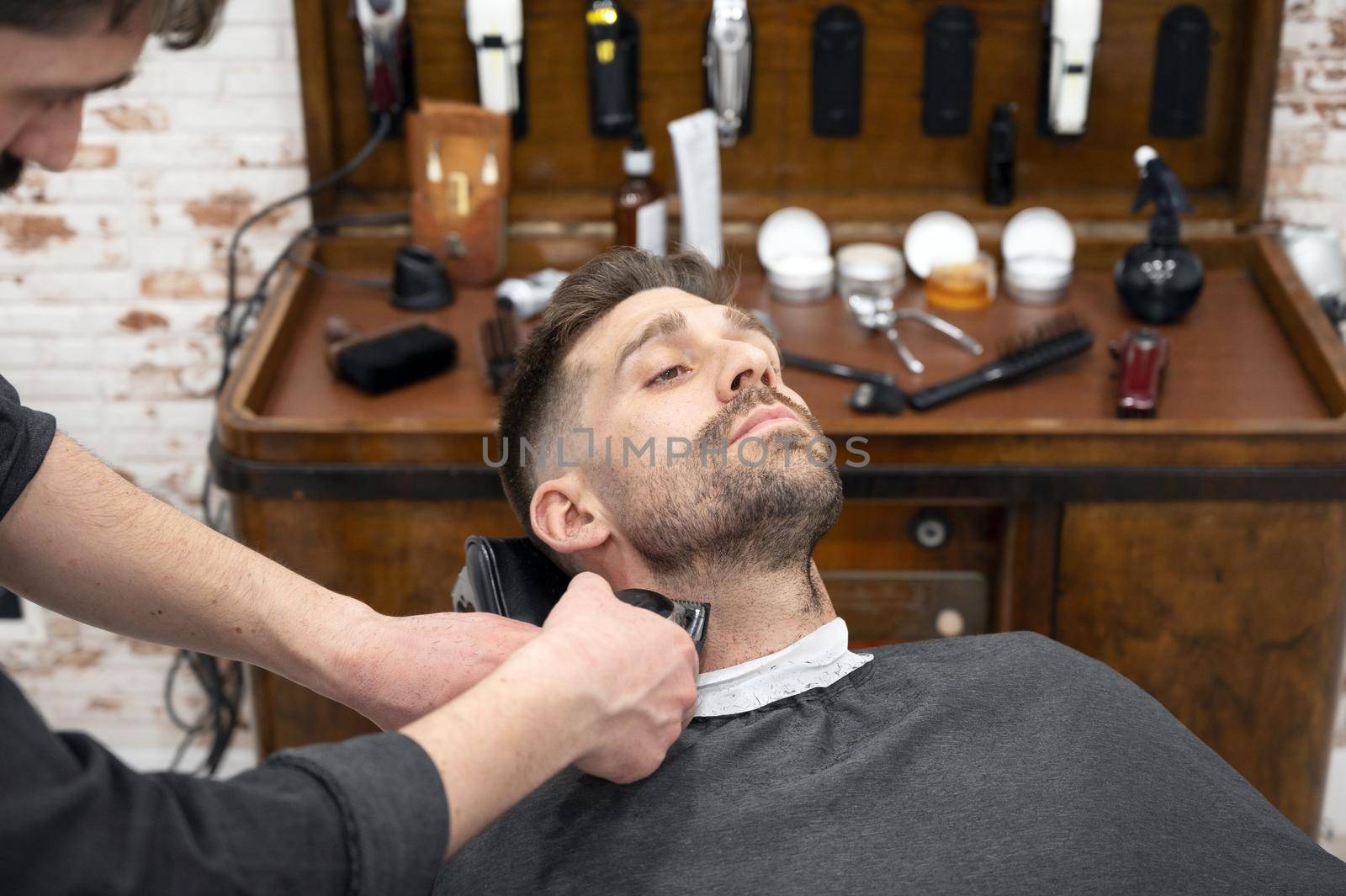Young hipster Caucasian man during beard grooming in modern barber shop. Men's hair styling. Handsome man getting new hairstyle with electric trimmer. High quality photography