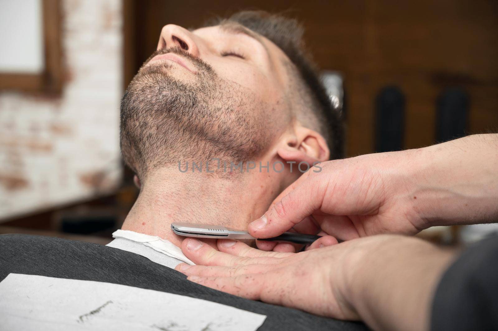 Barber shaving bearded male with a sharp razor. High quality photography