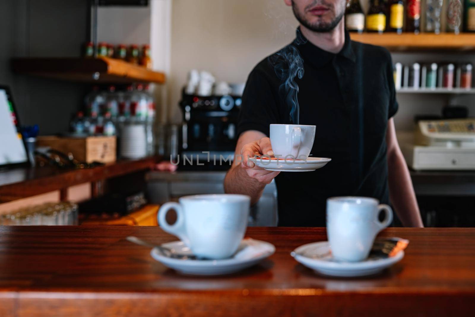 detail of a bar with two coffee cups. Waiter serving cups of coffee at the bar counter. Cups of coffee steaming. by CatPhotography