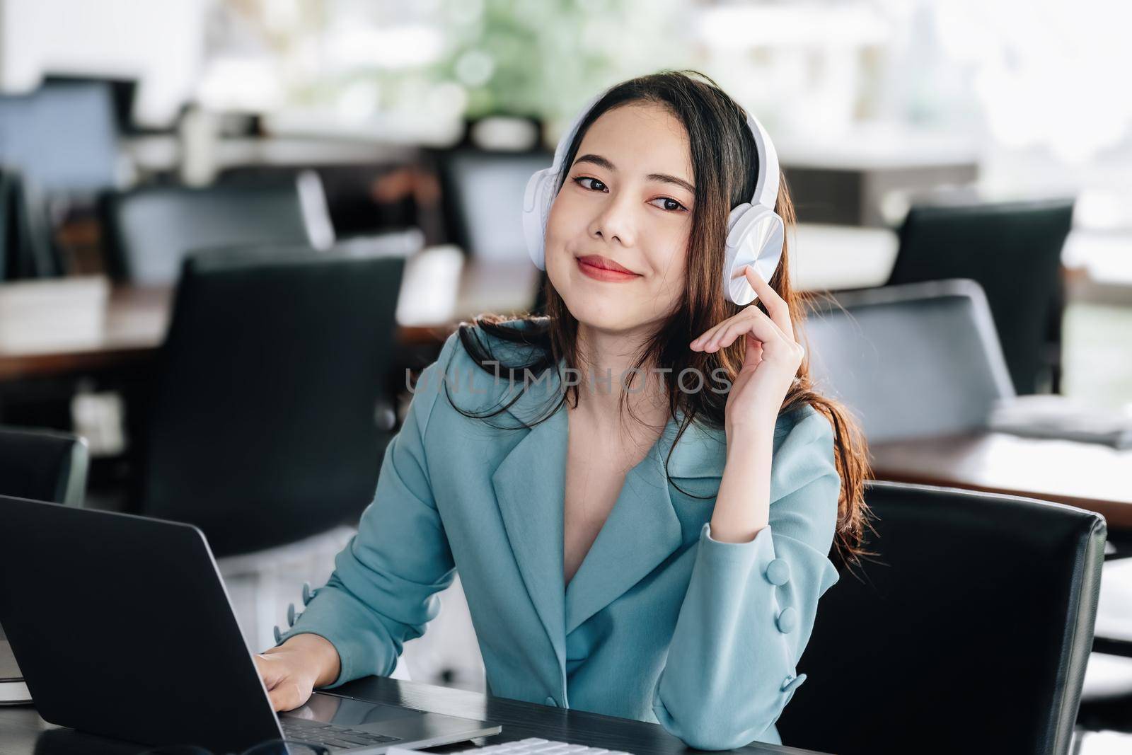 Asian female worker listening to music with smiling face to relieve stress while working at computer to rest her head and eyes