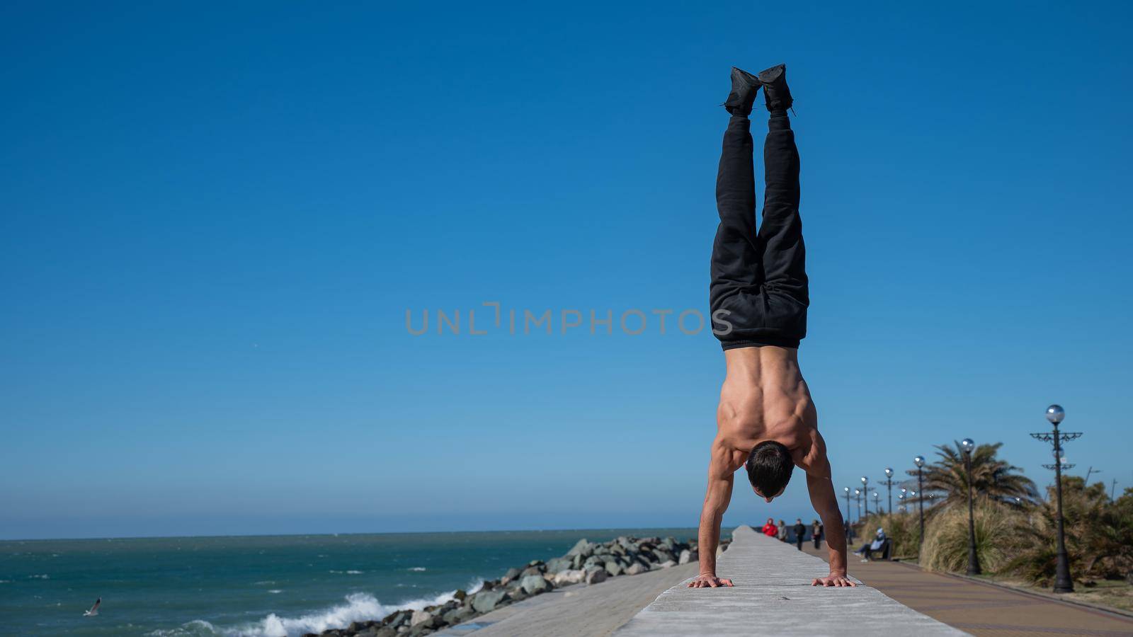 Shirtless man doing a handstand on the seashore. by mrwed54