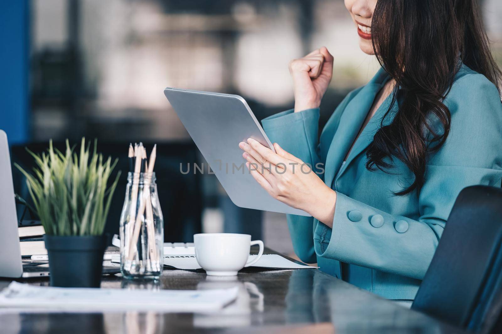 Business finance and investment, a business woman expresses happiness after successfully investing in the stock market on the Internet through a tablet placed on a desk. by Manastrong