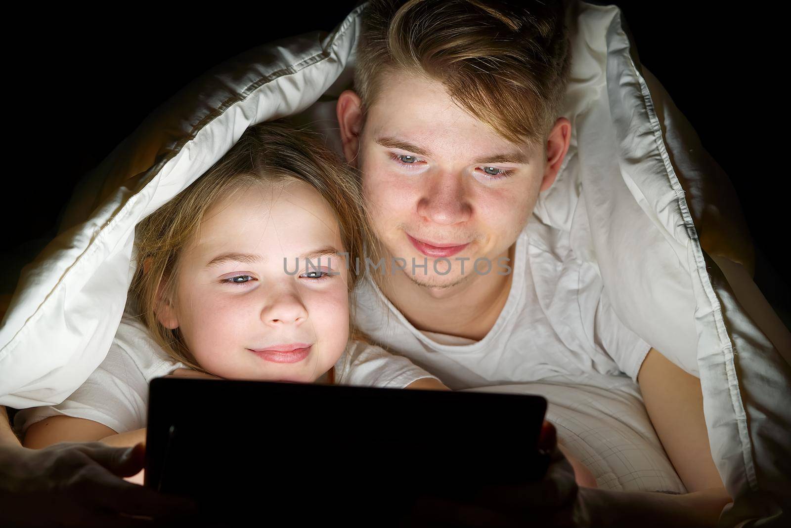 children play games on a tablet at night under a blanket, children watching video on tablet. communication through social networks. by PhotoTime