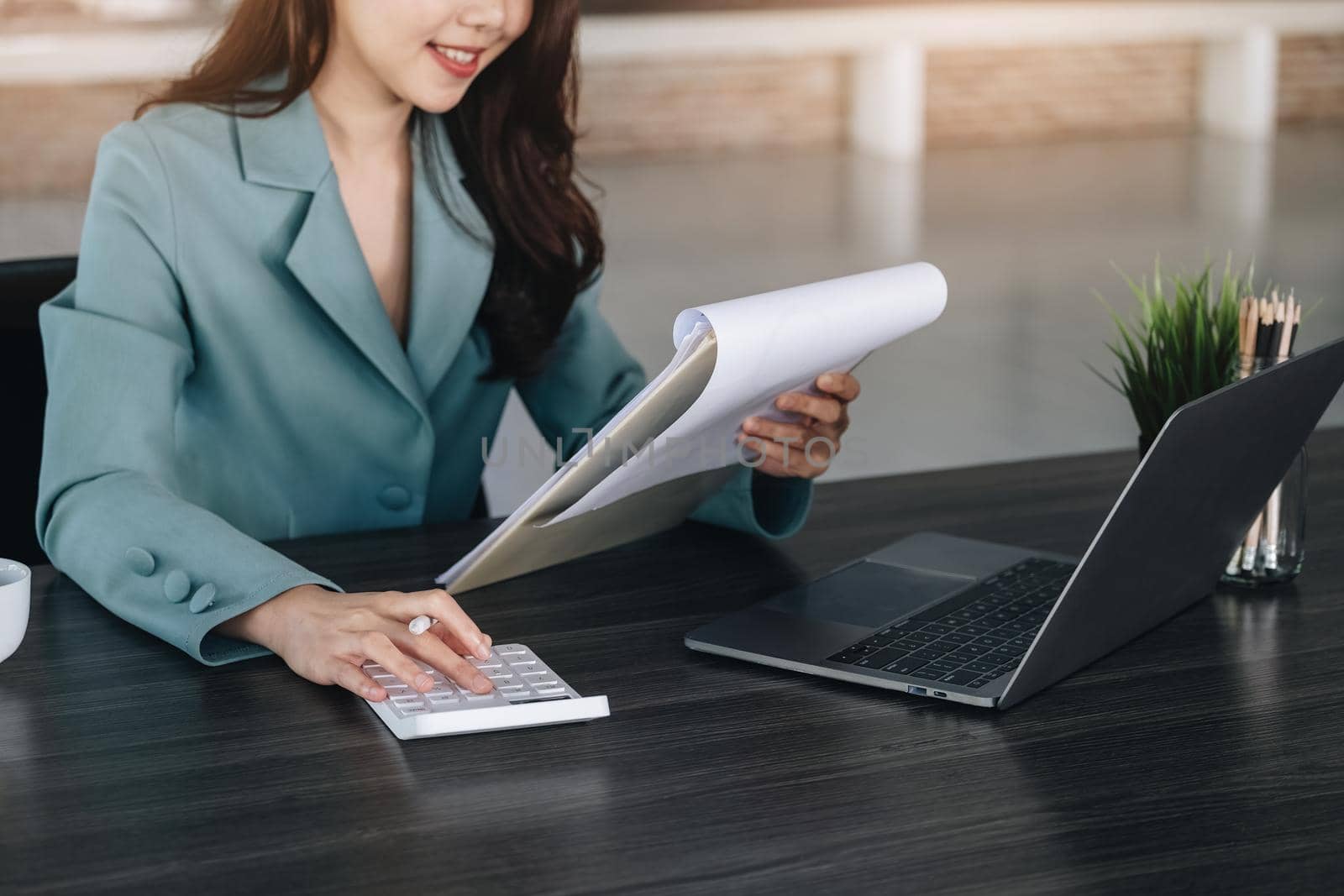 Financial and investment auditing concept, female auditor is pressing calculator to check budget and correctness of company profits through paperwork to calculate annual tax