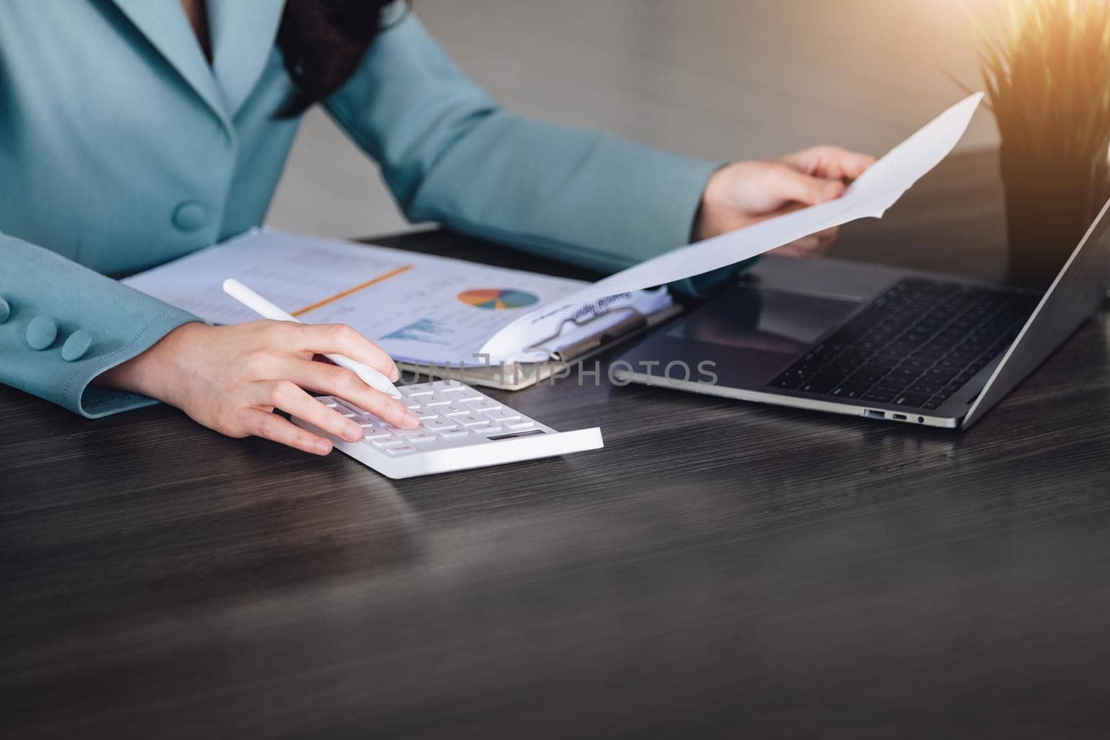 Financial and investment auditing concept, female auditor is pressing calculator to check budget and correctness of company profits through paperwork to calculate annual tax