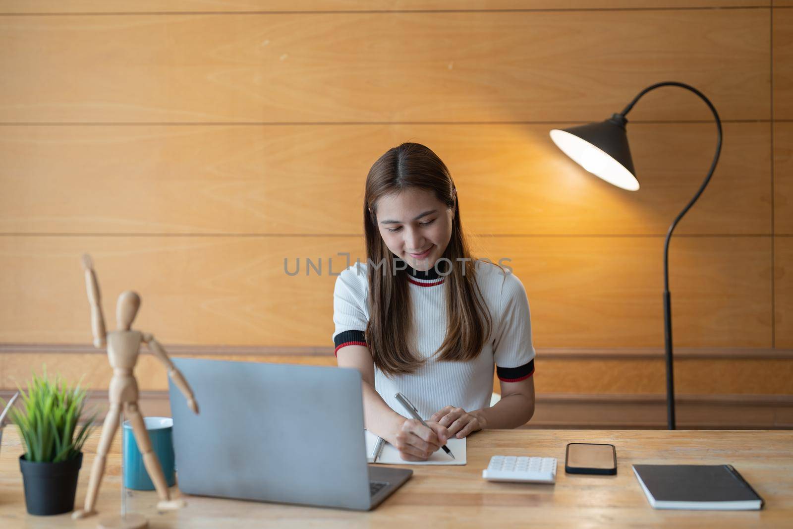 Young asian accountant taking note on notepad and using a laptop computer, calculator for financial