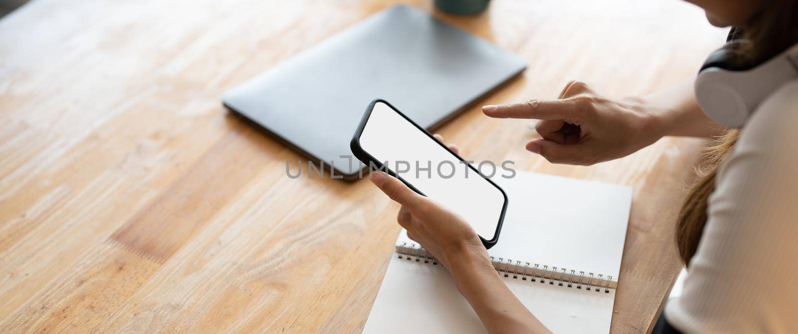 Top view Woman sitting and holding blank screen mock up mobile phone on wooden desk,