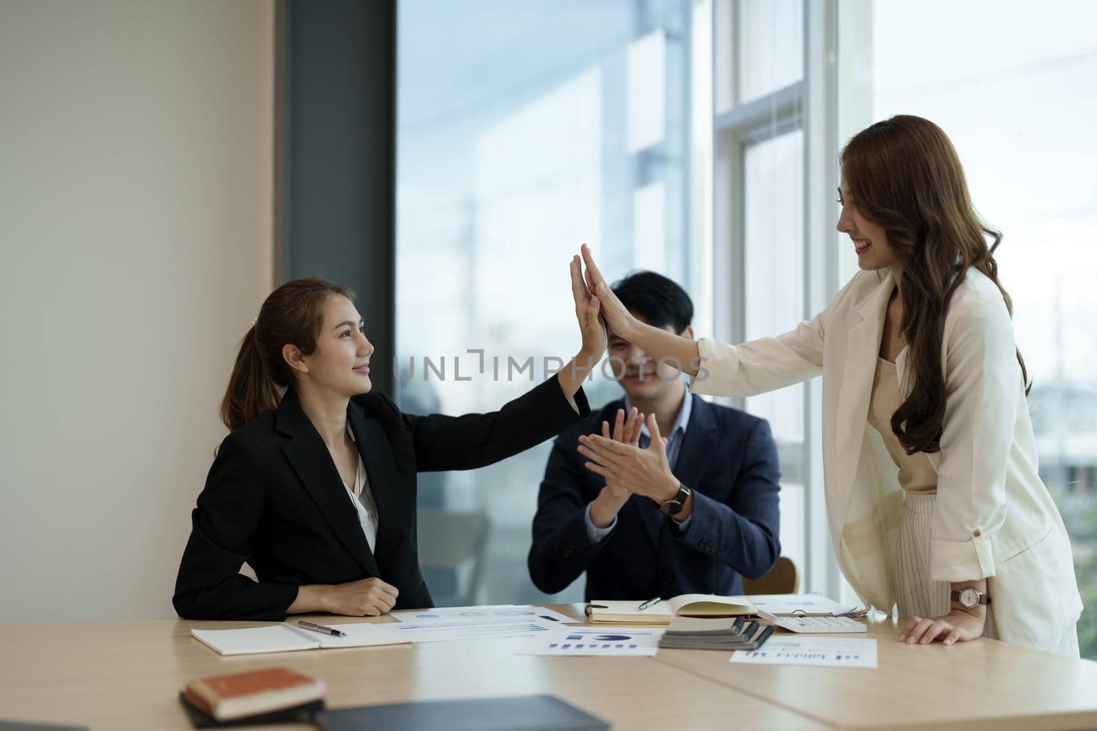 Diverse asian business team celebrating and giving high fives during boardroom meeting. business financial concept.