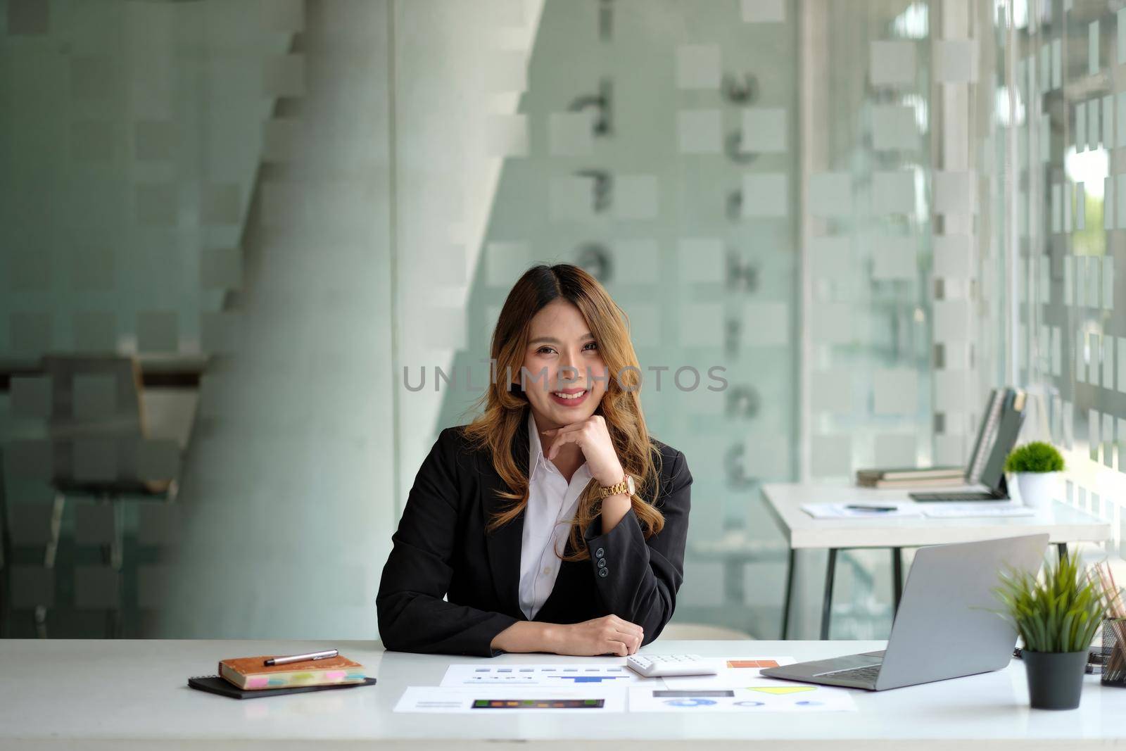 Portrait of attractive business woman sitting at her desk with laptop computer in office. Smiling business woman in black suit at office.