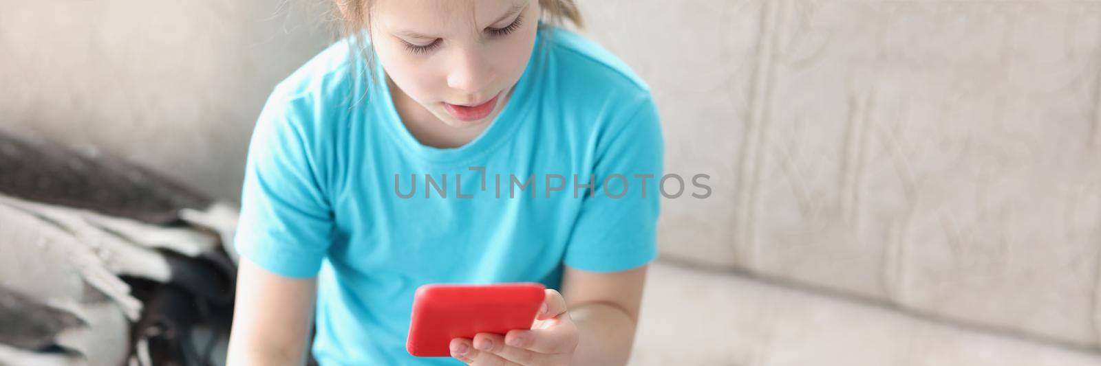 Top view of girl playing with smartphone, modern device in kid hands. Spend time in online games, addiction to technology from childhood. Pastime, kill time, fun concept