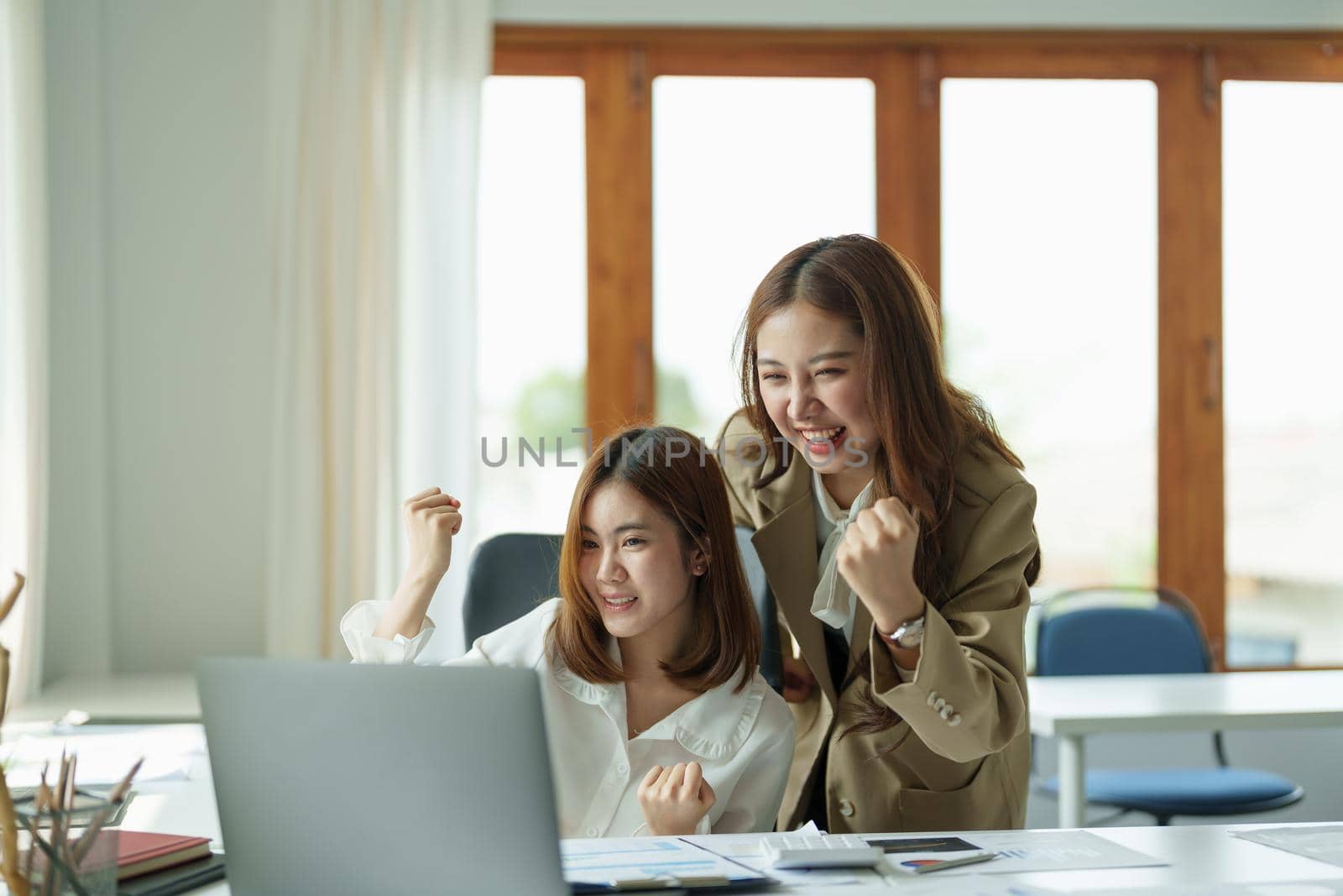 Happy young business asian team looking at laptop screen, celebrating success, Raising arms in a celebration of a successful