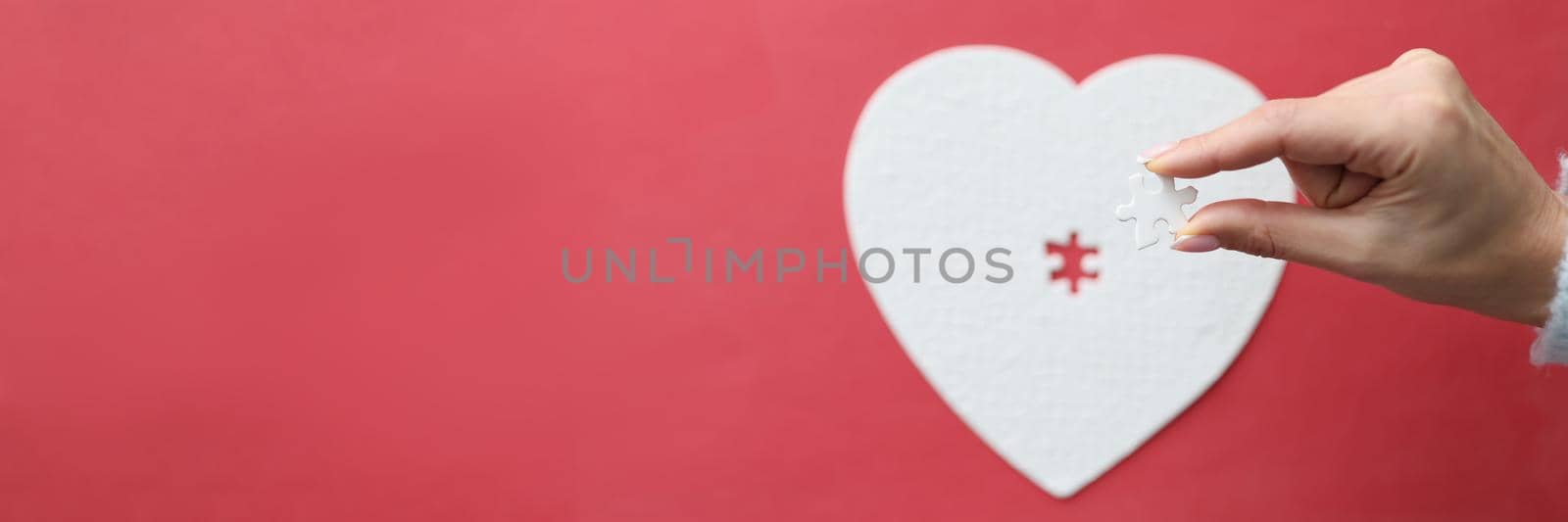 Top view of female hand holding missing piece of heart puzzle jigsaw. Love relationships concept. Copy space on left side. Isolated on pink background