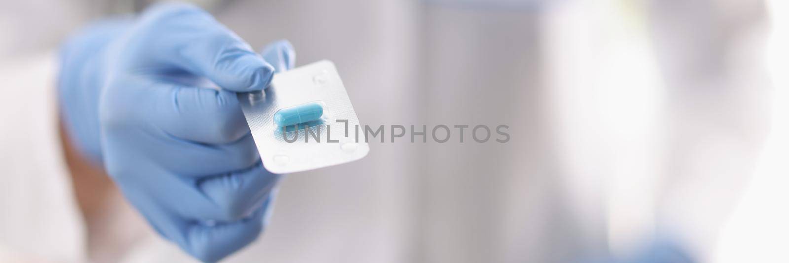 Close-up of practitioners hand in protective glove holding blue pill in blister. Pain relievers, vitamins or antibiotics for treatment. Medicine and healthcare concept