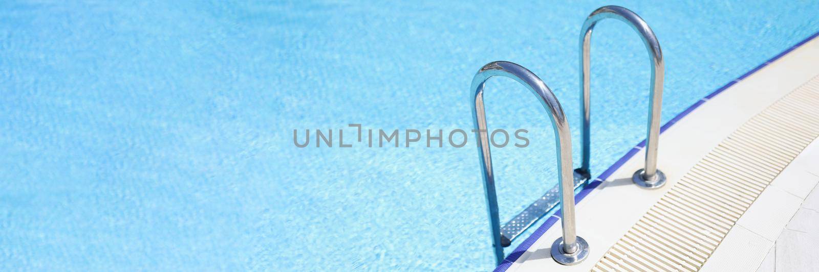 Close-up of empty swimming pool with stair at hotel, blue water and metal descent. Private territory in luxury accommodation. Rest, swimming, resort, summertime, holiday concept