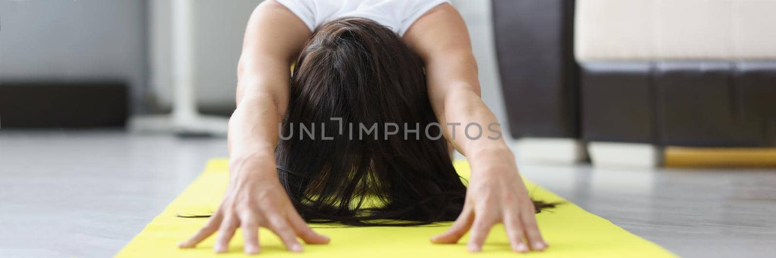 Close-up of woman practicing yoga doing tilts in seated forward bend pose, asana for stretching legs on mat at home. Sport, fitness, training, stretching, yoga and wellness concept